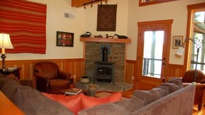 A cozy living room with a stone fireplace, leather armchairs, and a large window. - Goss Lake Chalet (Langley)