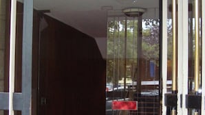A hotel entrance with a glass door, a dark interior visible through the door, and a metal gate with vertical bars. - B&B Piazza Ragusa (Rome)