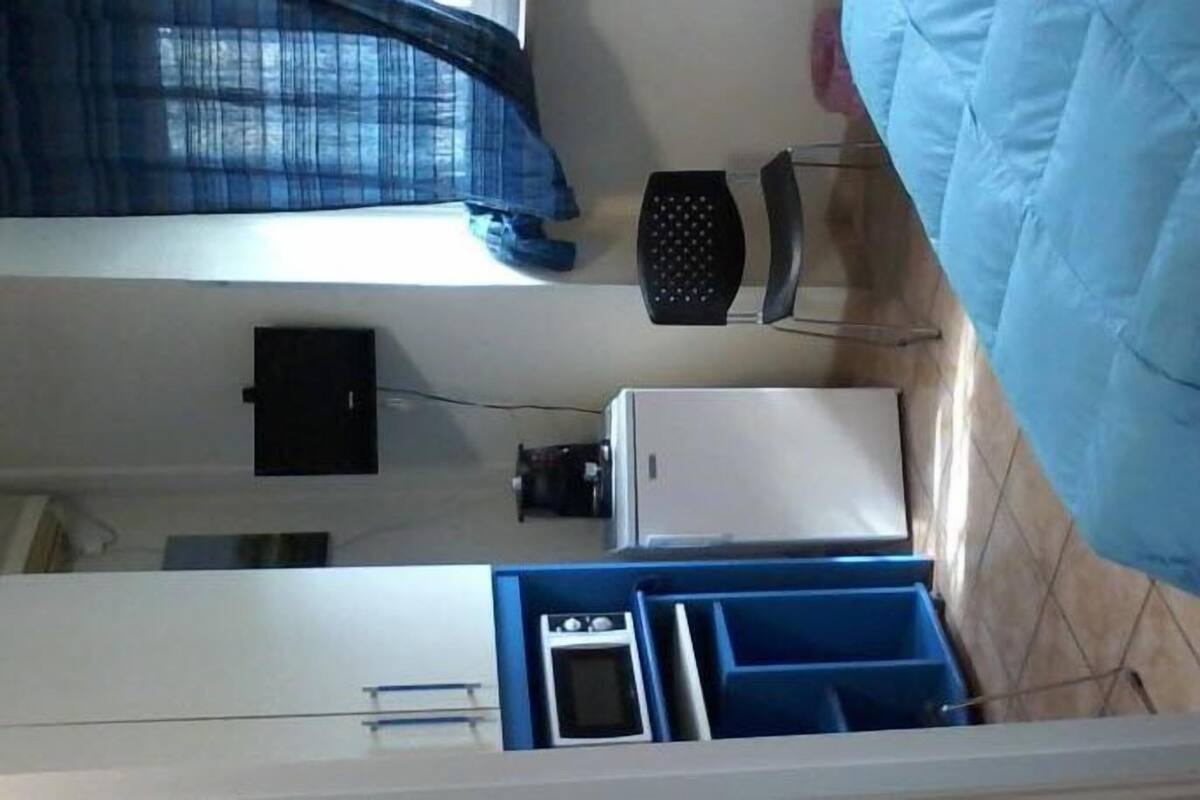 A compact kitchen with a refrigerator, stove, and blue storage bins.