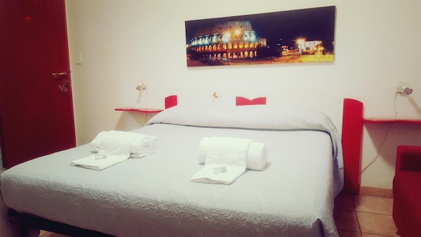 A neatly made bed with two rolled towels, a night light, and a framed picture of a building at night on the wall. - B&B Piazza Ragusa (Rome)