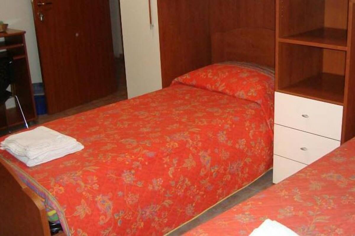 A bedroom with two beds, each with a floral-patterned bedspread and a white drawer unit.
