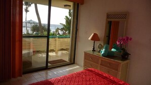 A bedroom with a bed, a dresser, a mirror, and a view of the beach through a sliding glass door. - 1612 Watergate (St. Thomas)