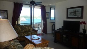 A living room with a sofa, a coffee table, a TV, and a view of the sea through large windows.