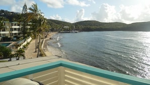 Blick auf den Strand mit Balkon, Palmen und einem Segelboot in der Ferne.
