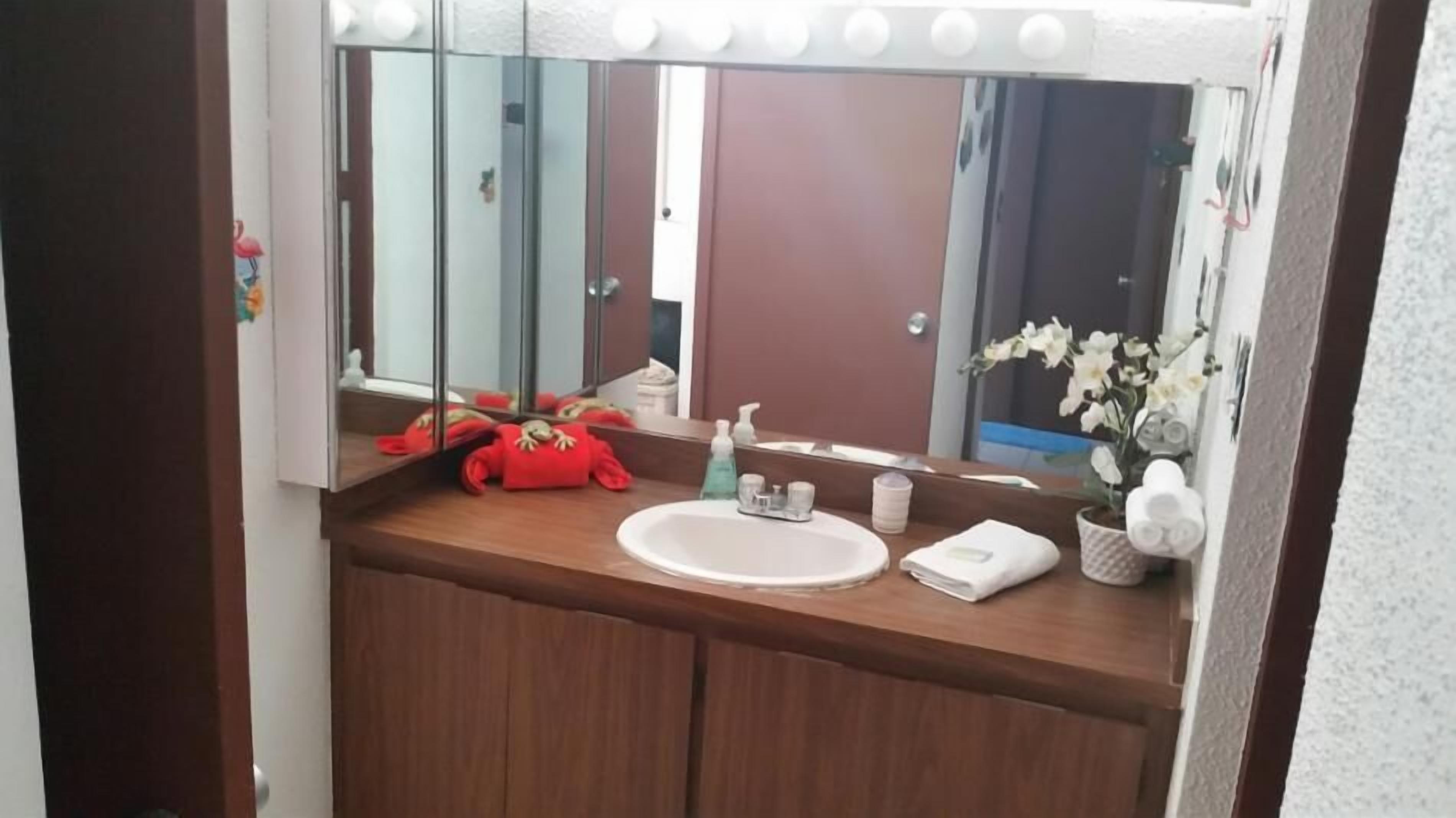 A bathroom with a wooden vanity, a white sink, and a large mirror with lights above it.