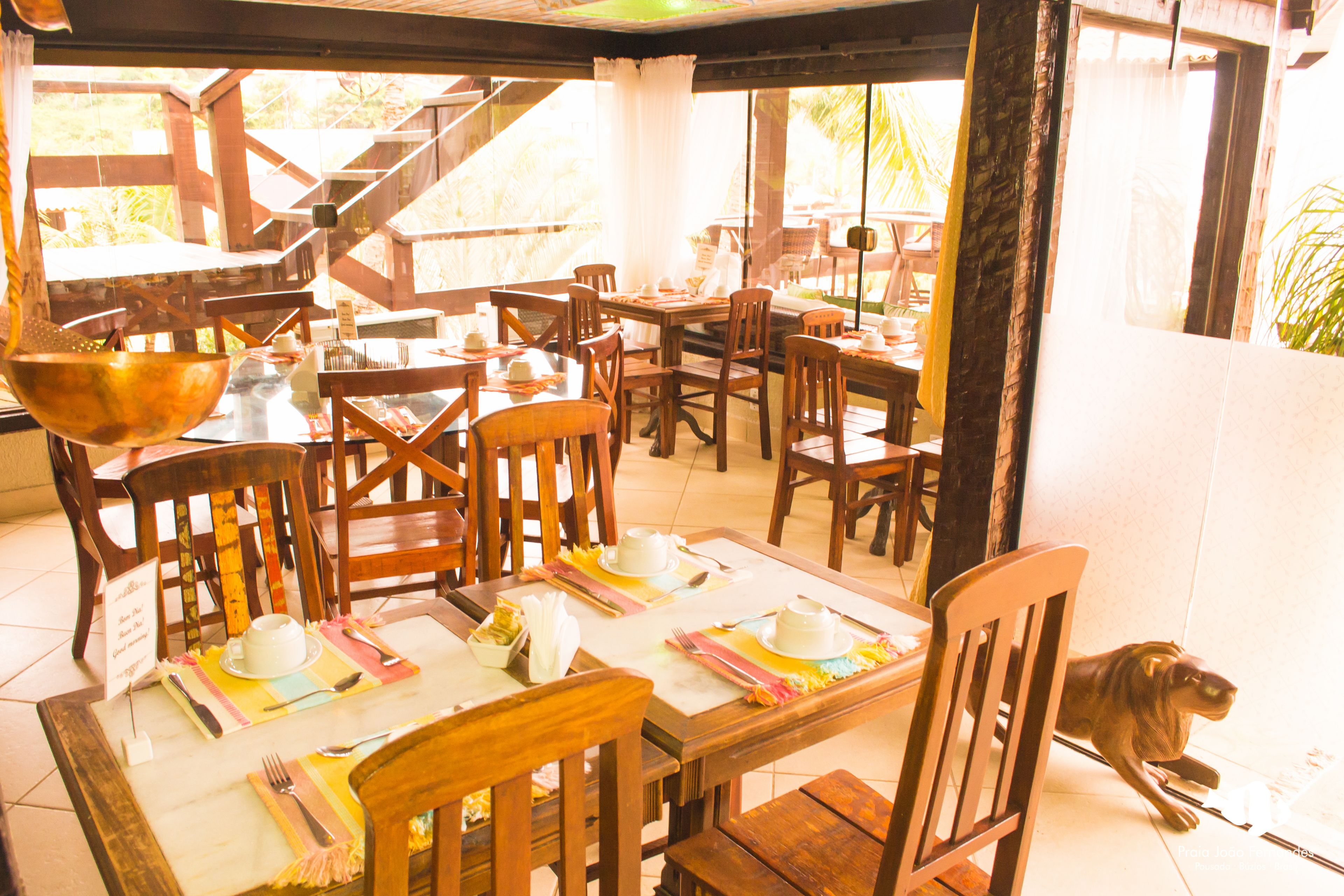 A restaurant with wooden tables and chairs, a dog on a leash, and a view of the outdoors.