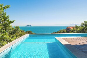 A clear blue pool with a wooden deck and a view of the sea and distant mountains. - Pousada Praia João Fernandes (Búzios)