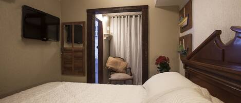 A hotel room with a bed, a chair, a TV, and a window with curtains.