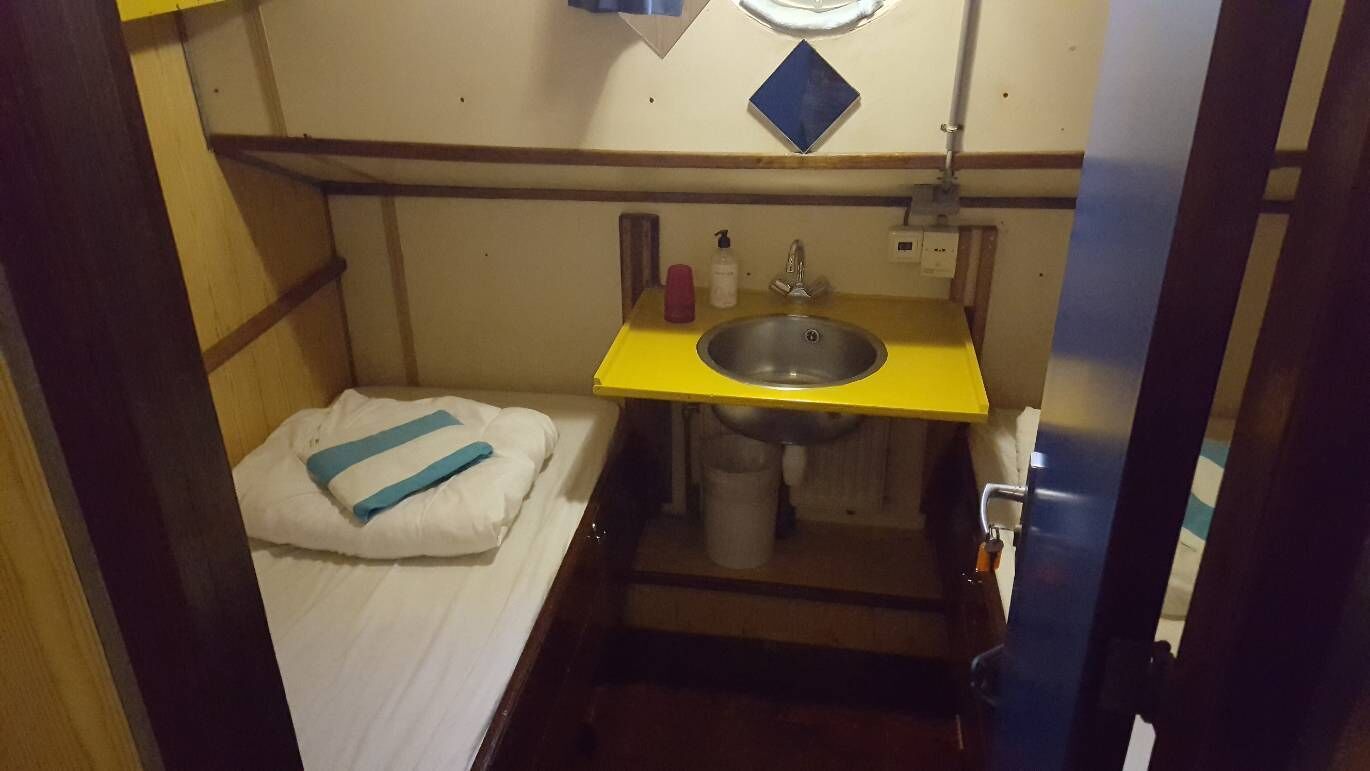 Una habitación pequeña y funcional con cama, lavamanos y espejo.