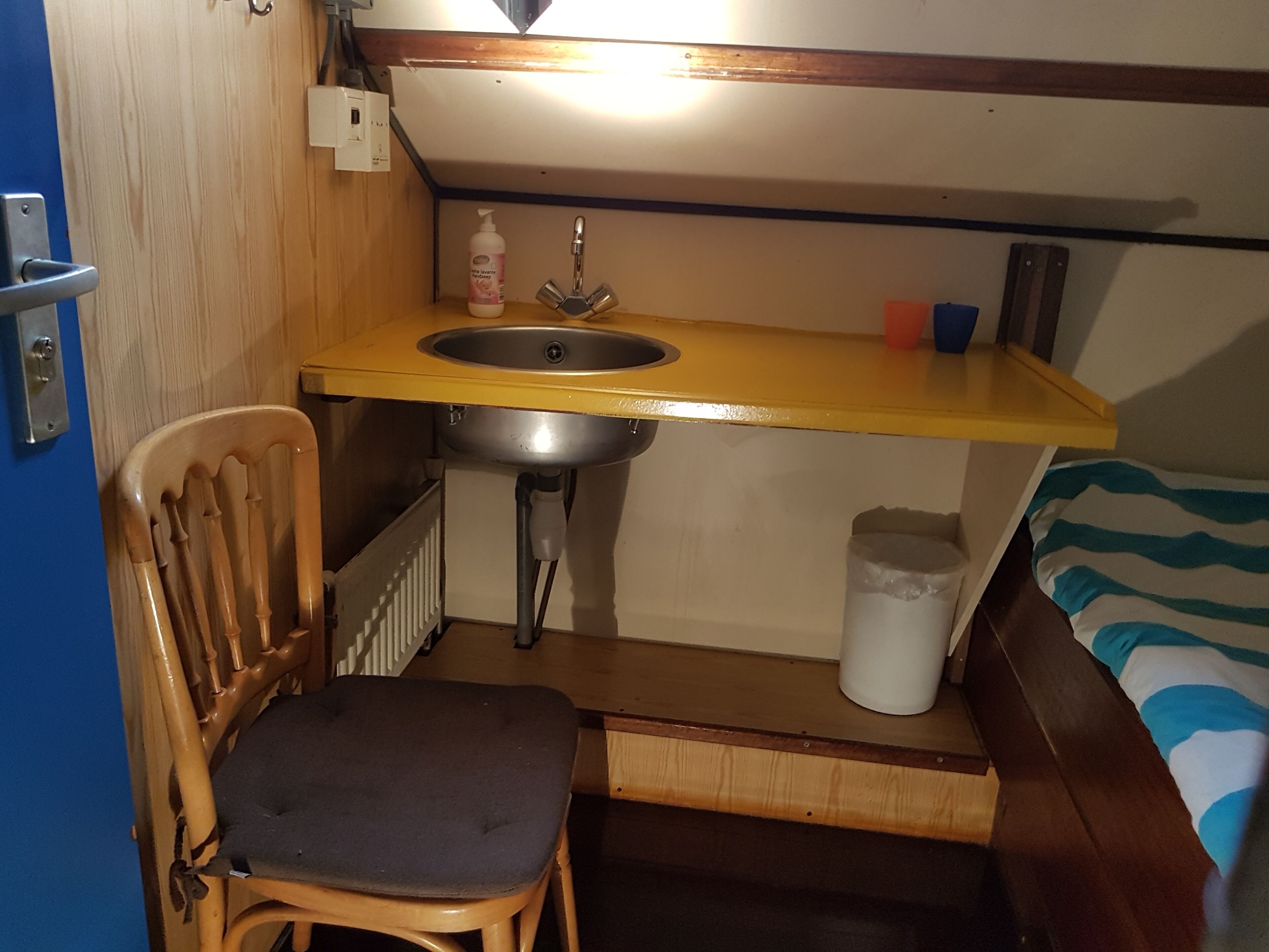 Una kitchenette pequeña con lavamanos, silla y estante de almacenamiento.