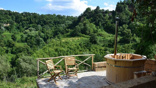 A stone deck with wooden chairs and a wooden hot tub overlooking a forested hillside. - Bio Agriturismo Valle dei Calanchi (Castiglione in Teverina)