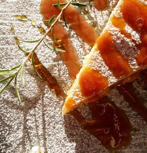 Eine Nahaufnahme eines Lebensmittels mit einer Puderbestreung, vermutlich ein Dessert, mit einem Rosmarinzweig daneben.