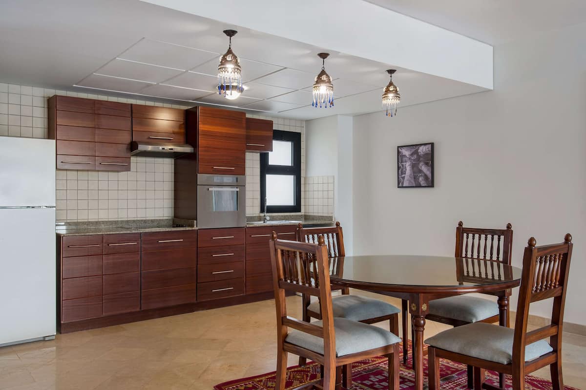 A modern kitchen with wooden cabinets, a stainless steel range hood, and a dining area with a round table and wooden chairs.