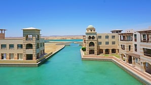 Un canal flanqueado por edificios, un puente a lo lejos y un cielo azul despejado.