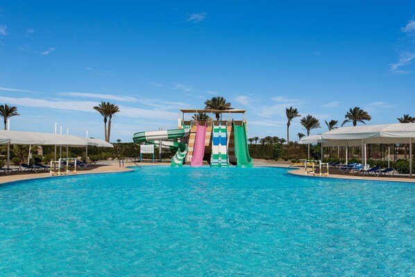 A swimming pool with a water slide, surrounded by palm trees and lounge chairs. - Marina Resort Port Ghalib Radisson Individuals (El Quseir)
