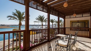 Un espacio al aire libre cubierto con vistas al puerto deportivo, que incluye una mesa, sillas, palmeras y una baranda de madera.