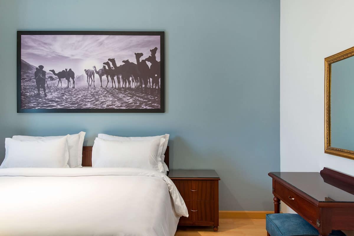A bedroom with a bed, a nightstand, a dresser, and a framed picture on the wall.