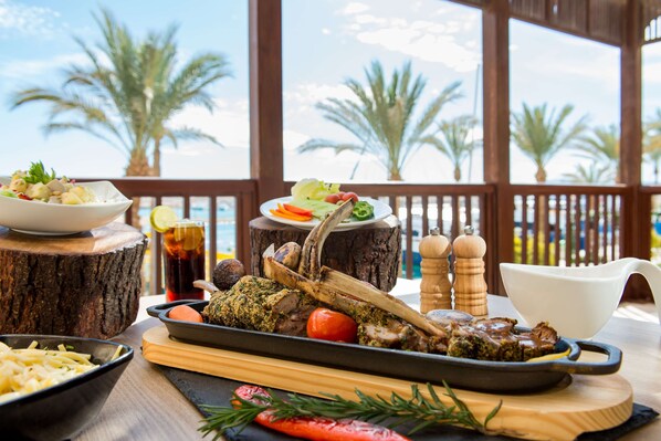 A dining table with a roasted lamb leg, a bowl of salad, and a glass of iced tea. - Marina Resort Port Ghalib Radisson Individuals (El Quseir)