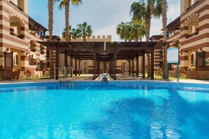 A swimming pool with a covered area and palm trees in the background. - Marina Resort Port Ghalib Radisson Individuals (El Quseir)