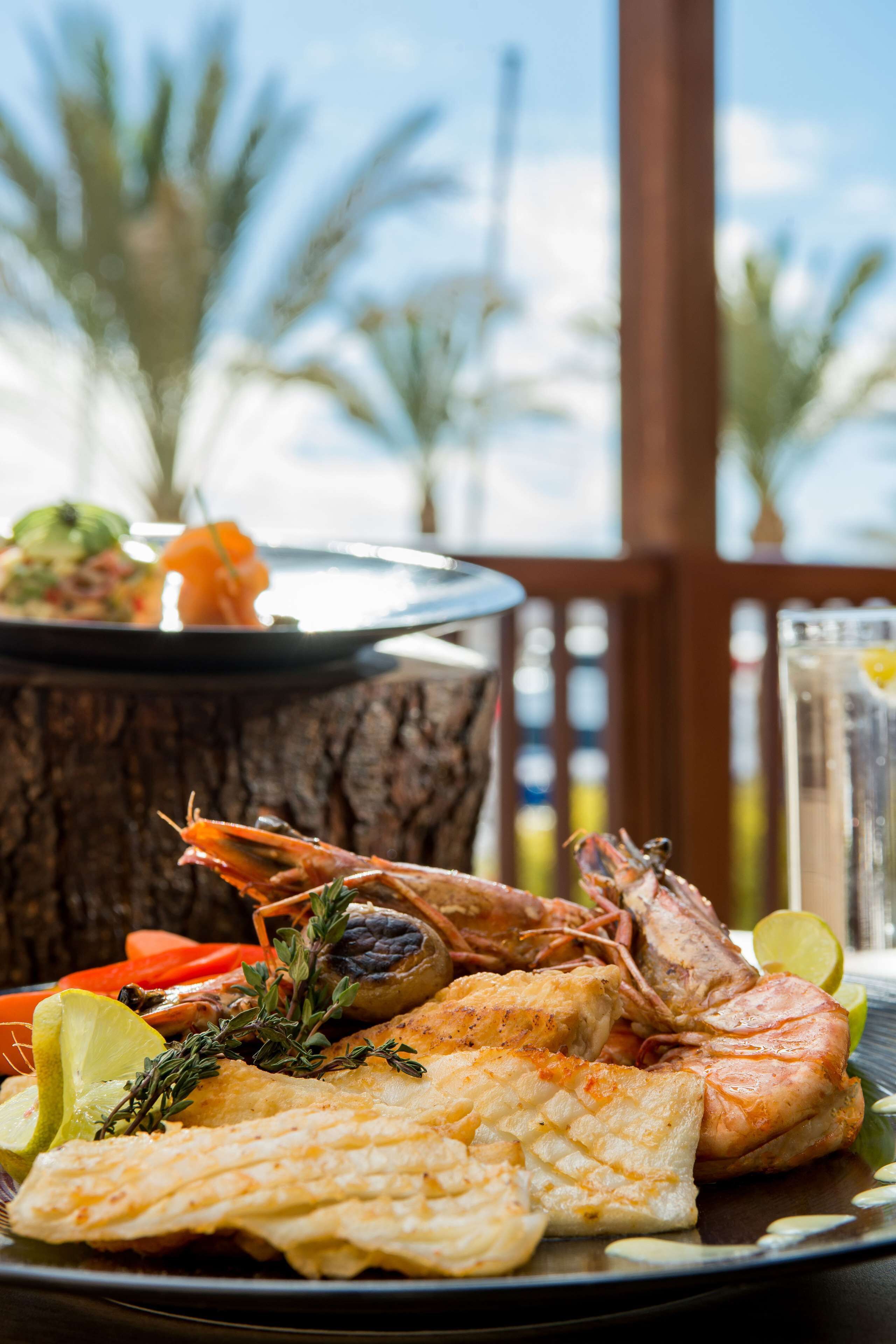 A seafood platter with shrimp, fish, and vegetables on a plate, with a tropical background.