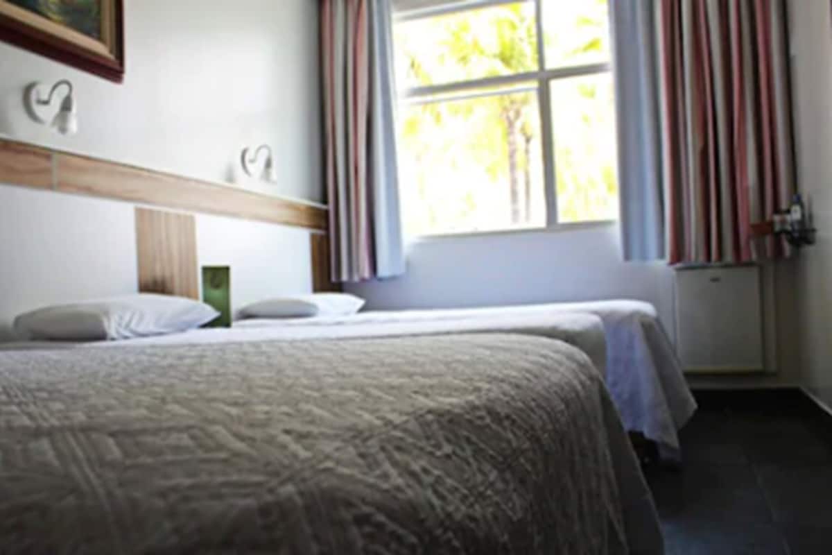 A hotel room with a large bed, a smaller bed, a window with curtains, and a radiator.