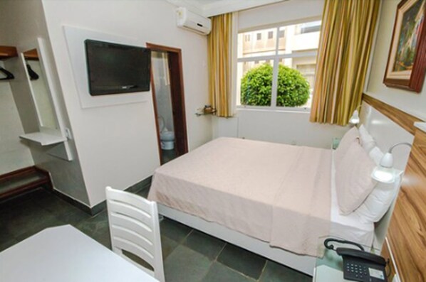 A hotel room with a bed, bedside table, lamp, and a phone.