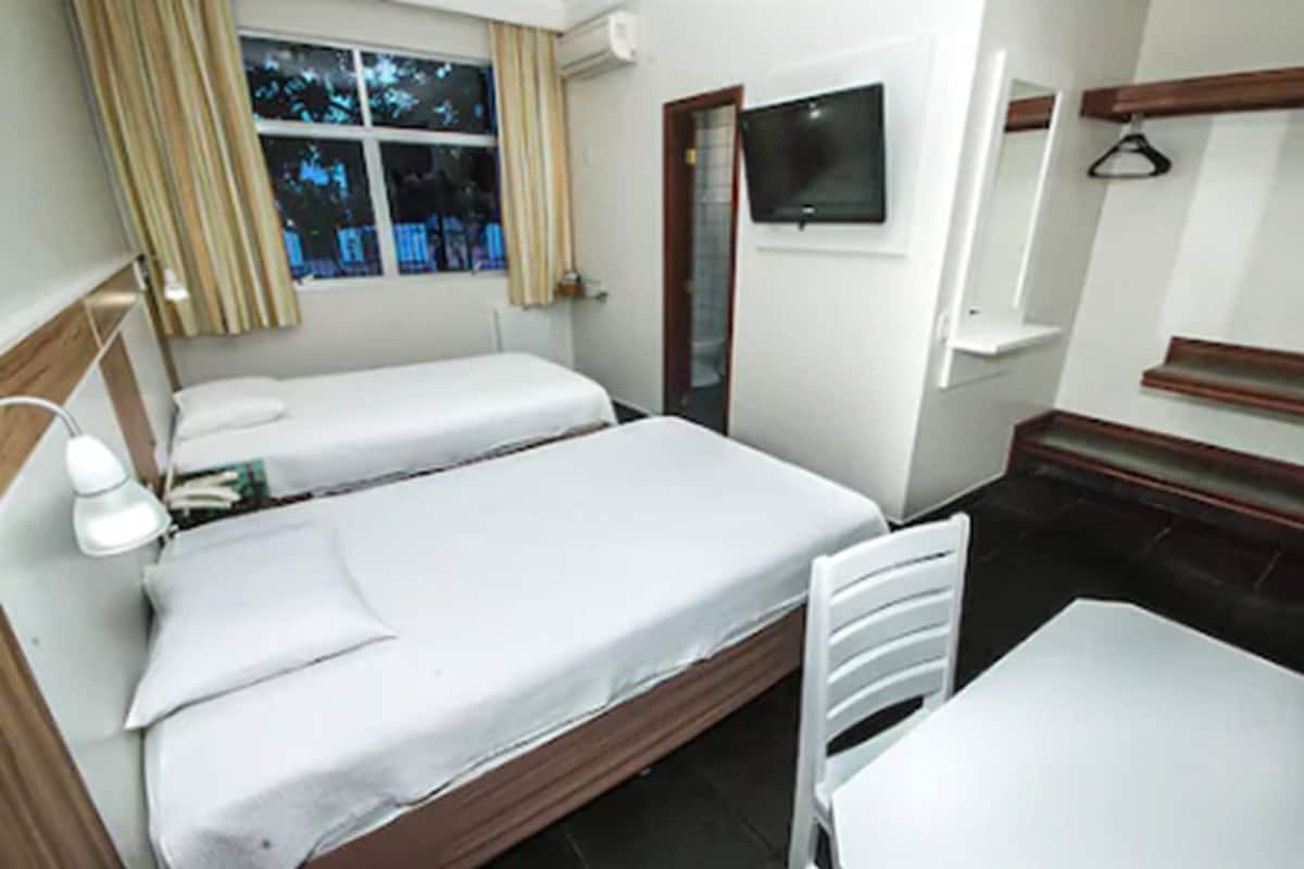 A small hotel room with two single beds, a TV mounted on the wall, a table, and a chair.
