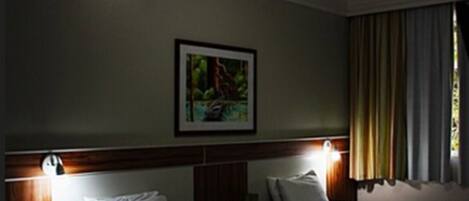 A hotel room with two beds, a framed picture on the wall, and curtains on the window.
