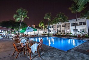A poolside area with lounge chairs and umbrellas, surrounded by palm trees and a building in the background. - Aipana Plaza Hotel (Boa Vista)