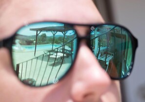 Primer plano de una persona con gafas de sol, donde se refleja una piscina y un puente.