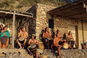 Un grupo de personas sentadas sobre escalones de piedra frente a un edificio de piedra con techo de madera, tocando la batería.