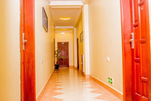 Un pasillo con puertas de madera a ambos lados, suelo de baldosas y un cuadro en la pared izquierda.