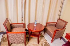 Una habitación con dos sillas de madera y una mesita redonda, una botella de agua sobre la mesa, y un tapete estampado en el suelo.