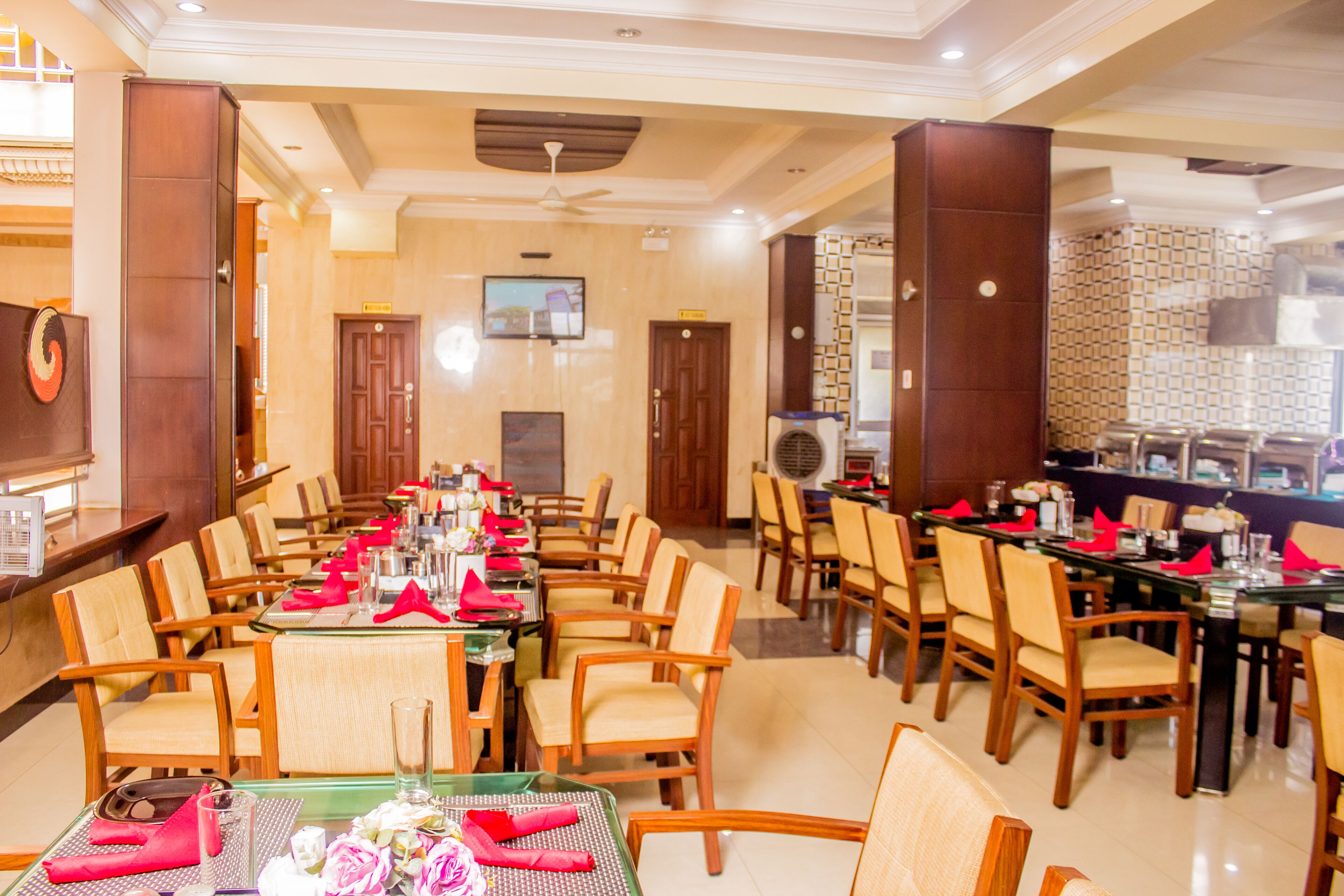A hotel dining area with multiple tables and chairs, a television on the wall, and a decorative wall pattern.