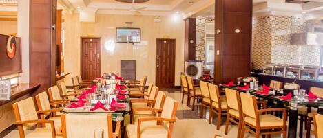 A hotel dining area with multiple tables and chairs, a television on the wall, and a decorative wall pattern.
