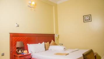 A hotel room with a bed, bedside table, lamp, and a framed picture on the wall.
