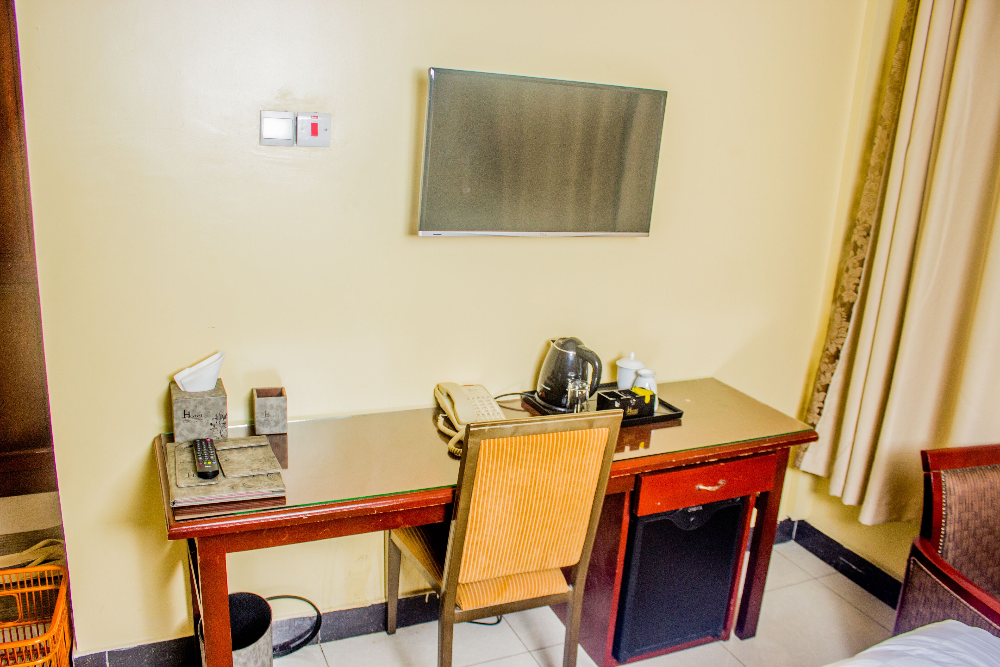 A hotel room with a desk, chair, bed, and a small table with a kettle and cups.
