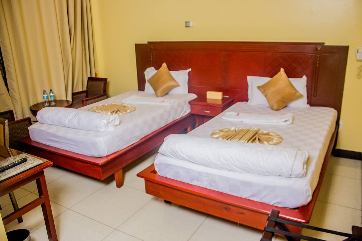 Two double beds with wooden headboards, a small table with a remote control, and a chair.