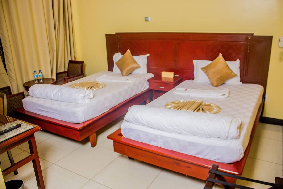 Two double beds with wooden headboards, a small table with a remote control, and a chair.