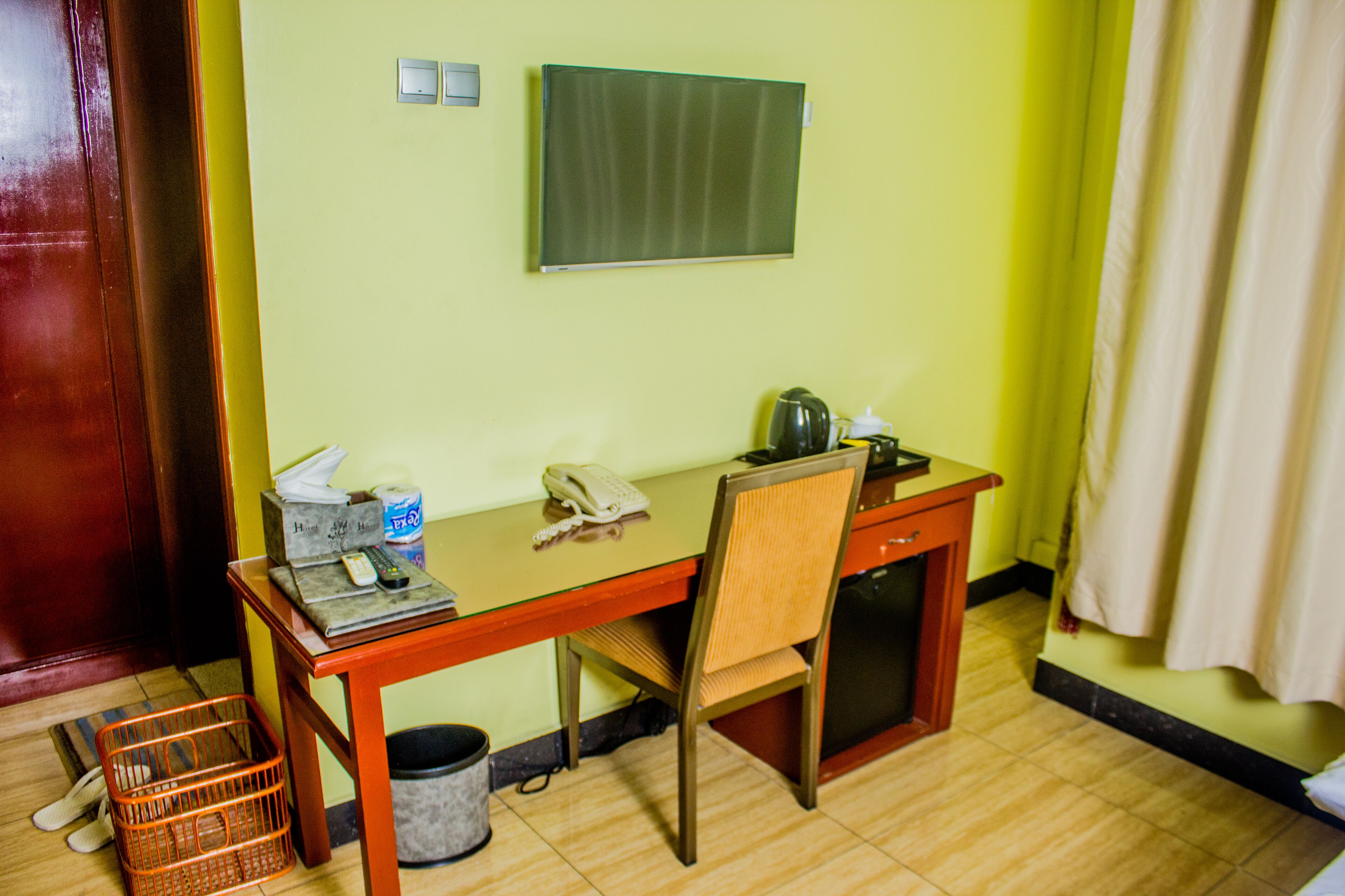 Een kleine kamer met een houten bureau, een stoel, een telefoon, een mand en een prullenbak.
