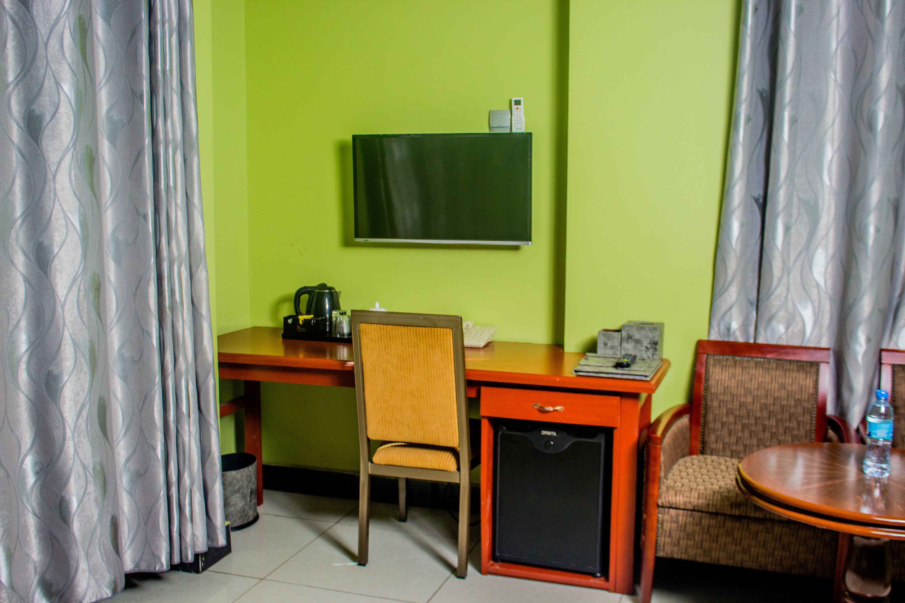 A room with a desk, chair, and a small table with a bottle.