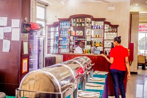 Zona de bar con mostrador, estantes llenos de bebidas y un bufé con platos cubiertos.