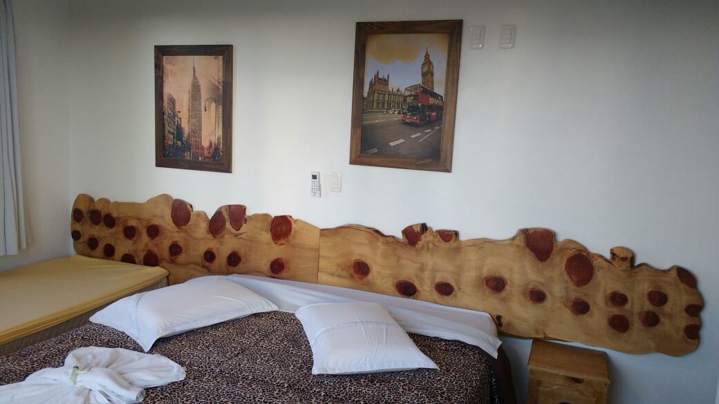 A hotel room with a unique wooden headboard, two paintings of cityscapes, a bed with white linens, and a small bedside table.