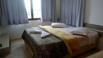 A hotel room with a bed, a bedside table, and a window with curtains.