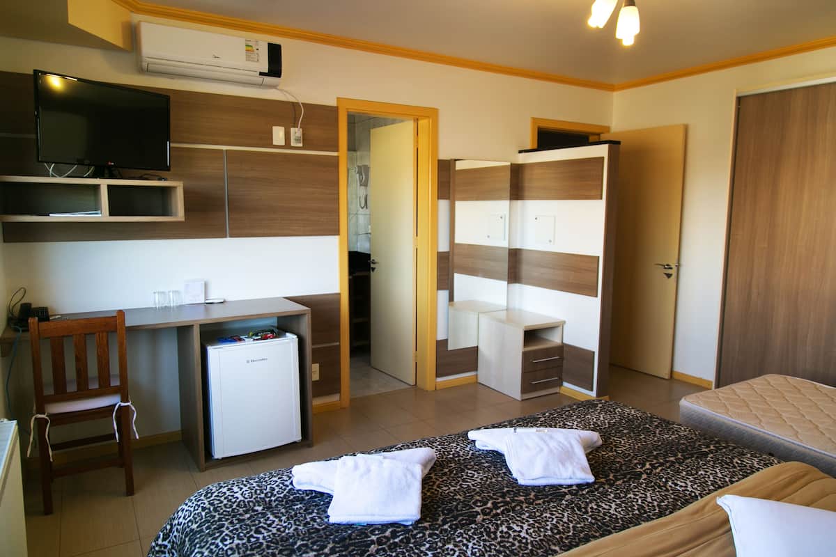 A hotel room with a bed, a desk, a chair, a television, and a wardrobe.