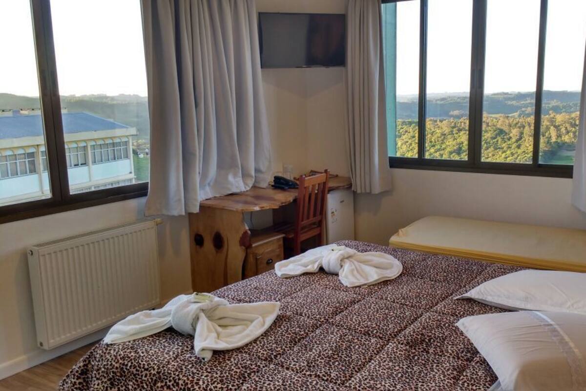 A bedroom with a bed, a desk, and a view of a forest through large windows.