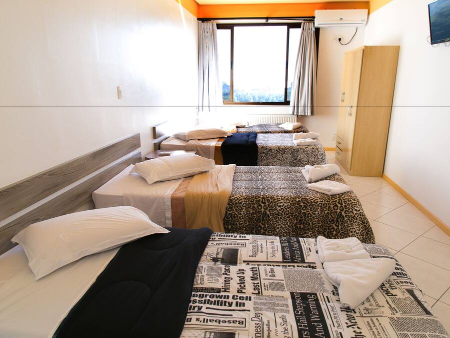 Habitación de hotel con tres camas, un armario y una ventana con cortinas.