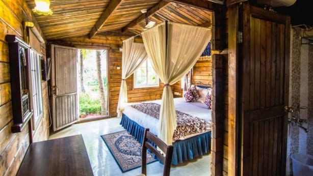 A wooden cabin bedroom with a bed, curtains, and a window. - Mahodadhi Palace (Puri)