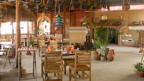 A restaurant with wooden tables and chairs, thatched roof, and potted plants. - Mahodadhi Palace (Puri)