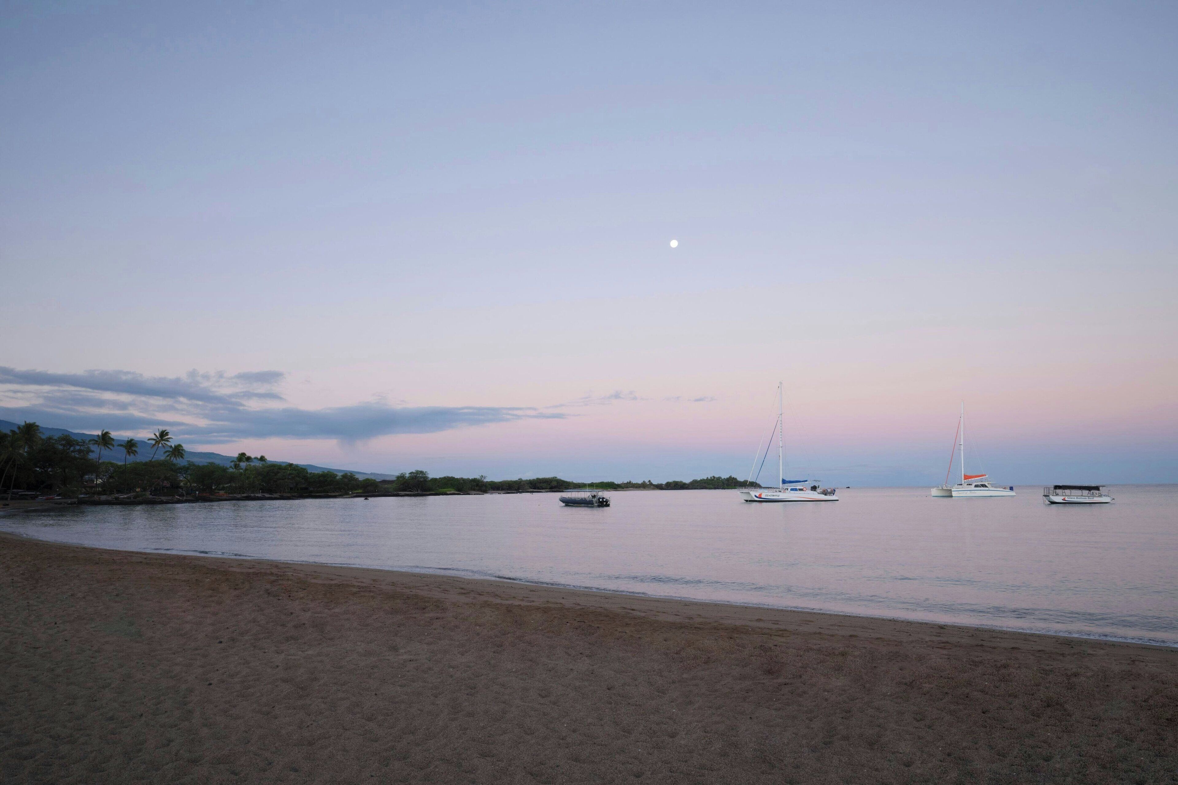 A beach with boats and a calm sea under a twilight sky.